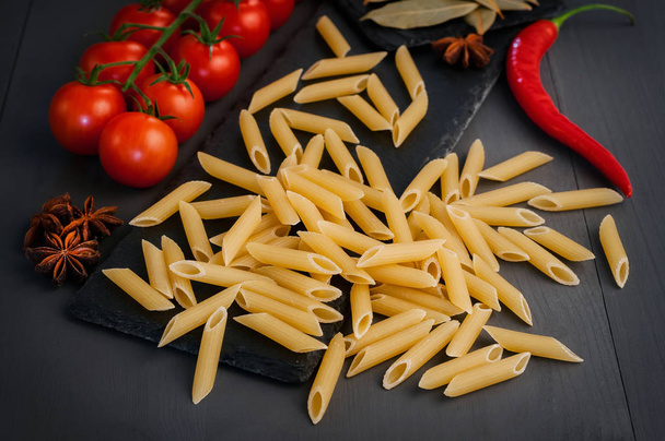 Macaroni sur un tableau noir sur fond gris avec tomates et piments forts
 - Photo, image