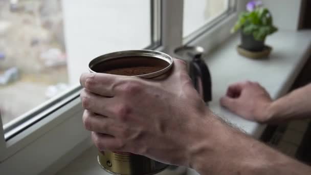 Close up shot of bearded young man sniffing ground coffee in a jar standing near a window in the kitchen - Video