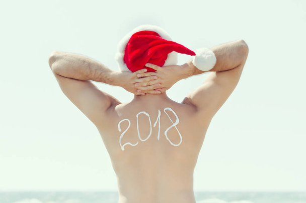 Man  in Santa's hat stands on the seashore. Hands behind his head - Photo, Image