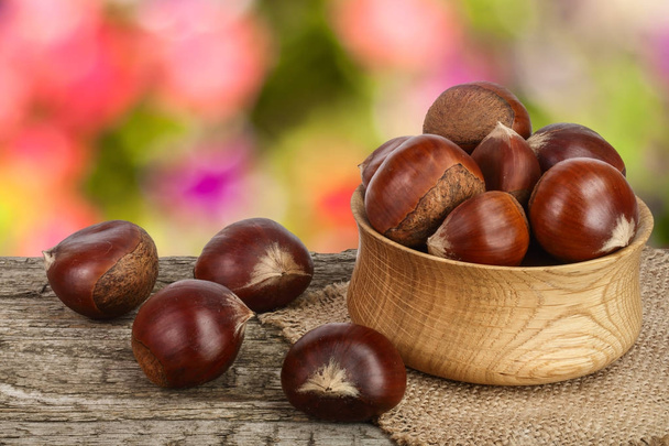 chestnut in bowl on the old wooden table with blurred garden background - Photo, Image
