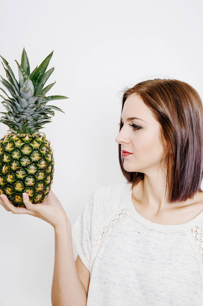 Dziewczyna trzyma ananasa. Młoda kobieta z ananasem. owoce i warzywa w ich rękach. ananas na głowie. - Zdjęcie, obraz