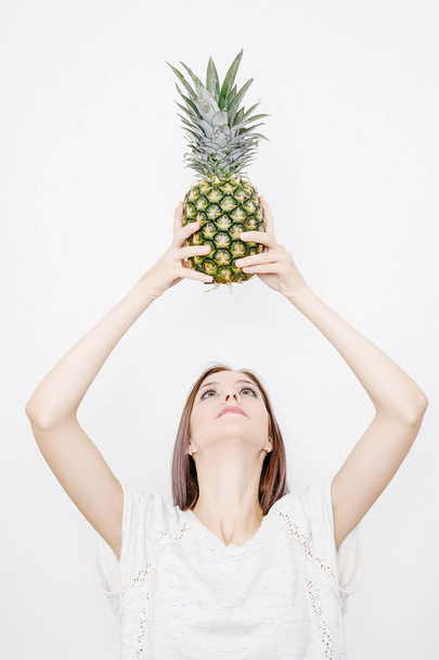 girl holds pineapple. Young woman with pineapple. fruits and vegetables in their hands. pineapple on the head. - Фото, зображення