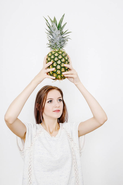 girl holds pineapple. Young woman with pineapple. fruits and vegetables in their hands. pineapple on the head. - Fotó, kép