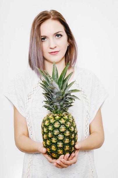 女の子は、パイナップルを保持しています。パイナップルと若い女性。果物や野菜を手に。頭の上のパイナップル. - 写真・画像