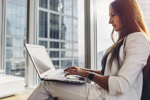 Side view of confident female entrepreneur using laptop sitting in modern business center - Photo, Image