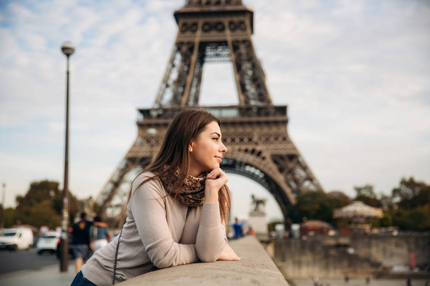 Krásná dívka pózuje fotografovi na pozadí Eiffelovy věže. Podzimní focení. Slunečné počasí. Krásný úsměv a make-up - Fotografie, Obrázek