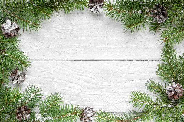 Christmas frame made of fir branches and pine cones on white wooden table - Photo, Image