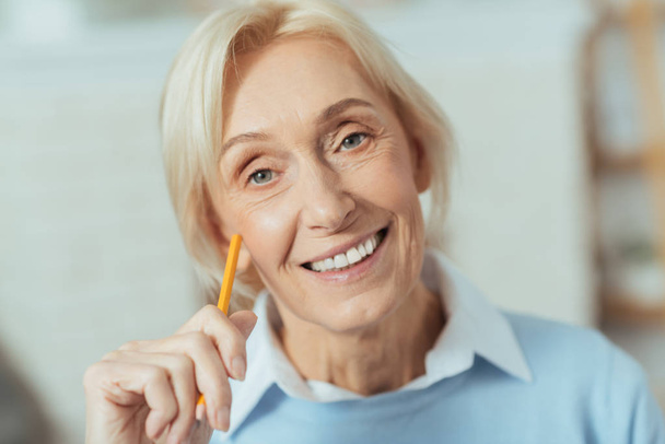 Positive pensioner smiling while holding a yellow pencil - Fotó, kép