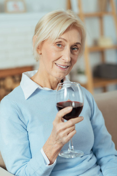 Happy aged woman drinking red wine and smiling kindly - Foto, Imagen