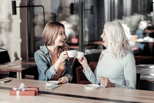 Excited women of different age sitting and drinking coffee together - Foto, imagen