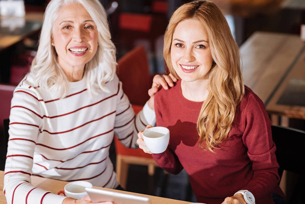 Mulher idosa alegre sorrindo enquanto sentada em um café com sua neta
 - Foto, Imagem