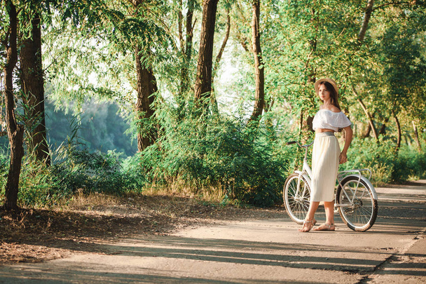 Ένα κορίτσι στέκεται κλίνει σε ένα ποδήλατο στο πάρκο - Φωτογραφία, εικόνα