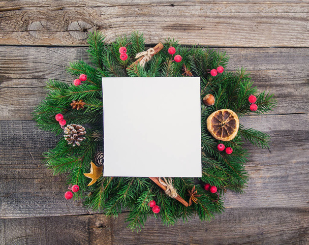 Christmas wreath with natural decorations - berries, cones, candied oranges, cinnamon, anise with square empty paper card with copy space inside. Old Rustic wooden background. - Photo, image