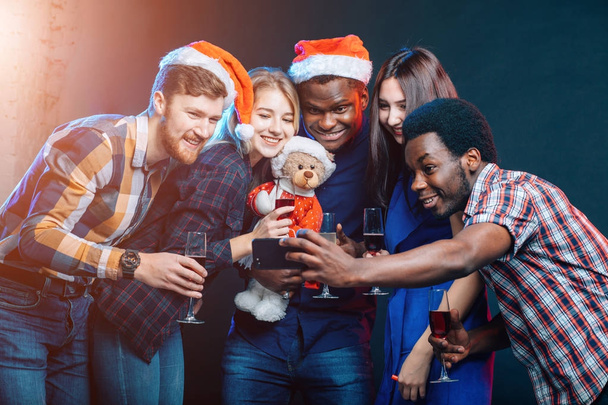 girls and guys in Santa hats doing selfie at party. Christmas, new year concept - Fotografie, Obrázek