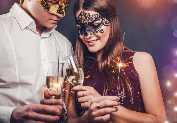 Pareja celebrando la víspera de Año Nuevo bebiendo champán e iluminando los bengalas en la fiesta de disfraces
 - Foto, imagen