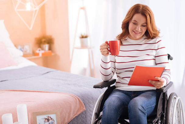 Alert smiling disabled woman holding a cup and a notebook - Фото, изображение