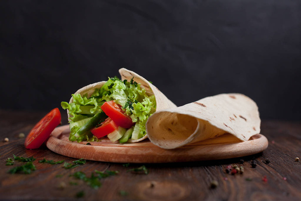  burrito with greens, cucumbers, tomatoes and sausages on a round wooden board on a wooden background - Fotografie, Obrázek