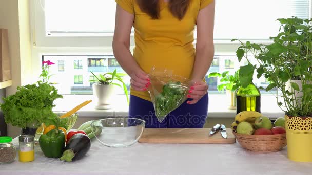 Mujer embarazada unbox hojas de ensalada verde y poner en plato de vidrio en la mesa de la cocina
 - Metraje, vídeo