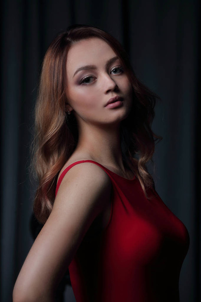 Charming brunette in a red dress posing on a black background. - 写真・画像