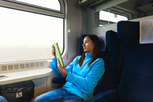 Enjoying travel. Woman traveling by train sitting near the window with tablet - Foto, imagen