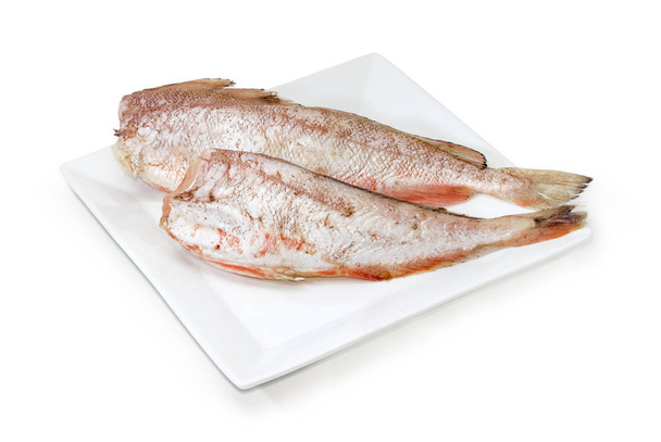 Duas carcaças de bacalhau vermelho não cozido em prato branco
 - Foto, Imagem