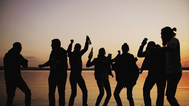 Silhouet van een groep jonge mensen dansen hebben een partij op strand op zonsondergang - Foto, afbeelding