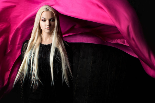 Stylish blonde on a dark background with bright flying fabric, color pink - Fotoğraf, Görsel