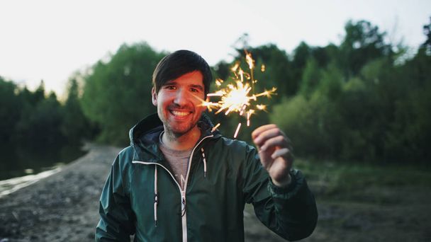 Portrait of young smiling man with sparkler celebrating at beach party - Photo, image