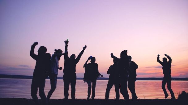 Ryhmän siluetti nuorilla tanssijoilla on juhlat rannalla auringonlaskun aikaan
 - Valokuva, kuva