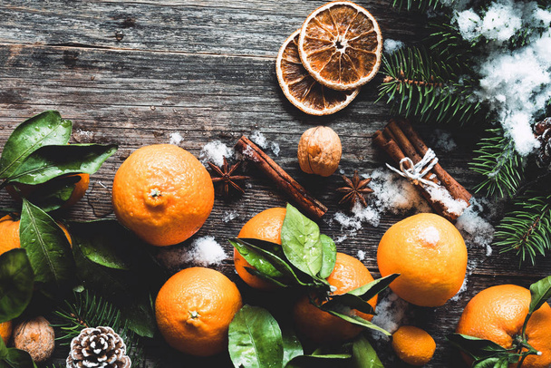 Traditional Christmas background with fir tree, tangerines, cinnamon and natural snow on wooden background - Foto, imagen