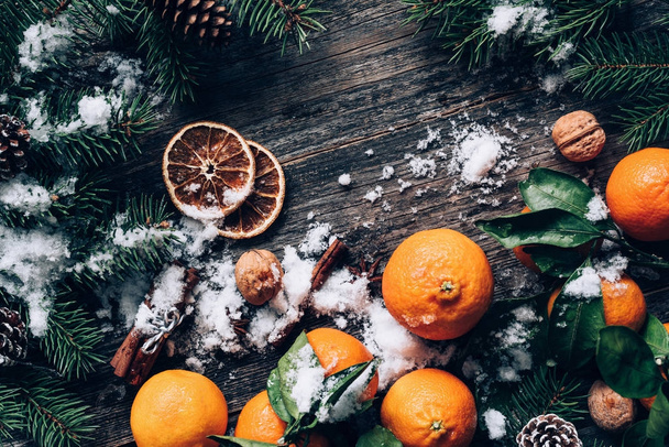 Christmas or New Year wallpaper background with tangerines, fir tree, spices and snow - Photo, image