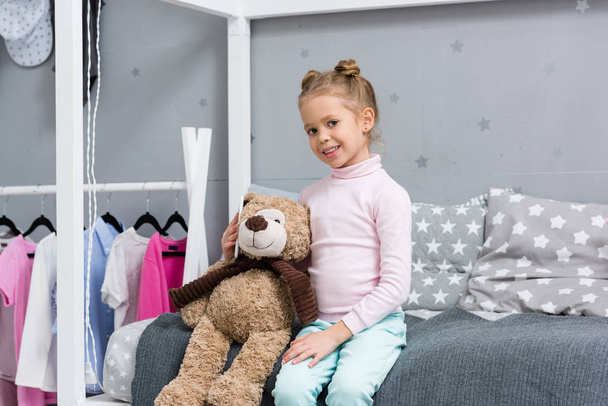 happy little kid sitting in bed with teddy bear - Foto, afbeelding