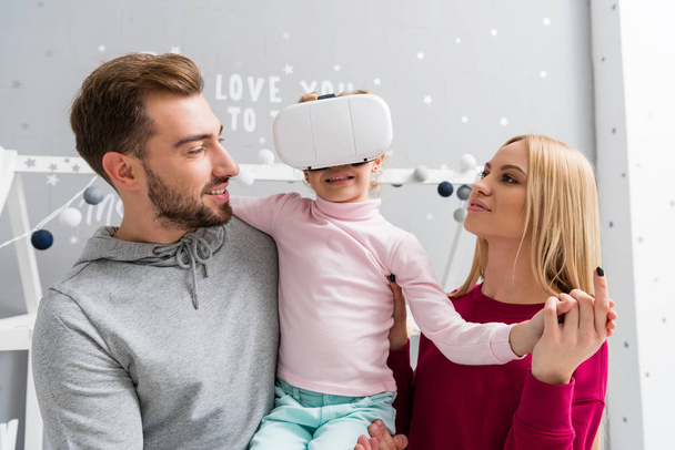 батьки дивляться на маленьку доньку, коли вона використовує гарнітуру віртуальної реальності
 - Фото, зображення