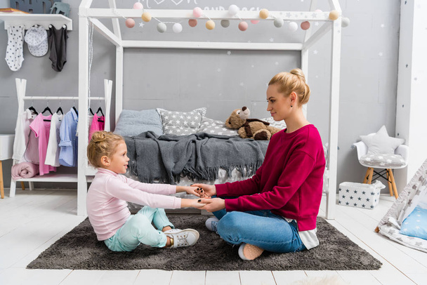 mother and daughter sitting on floor on kid bedroom and holding hands - Photo, image