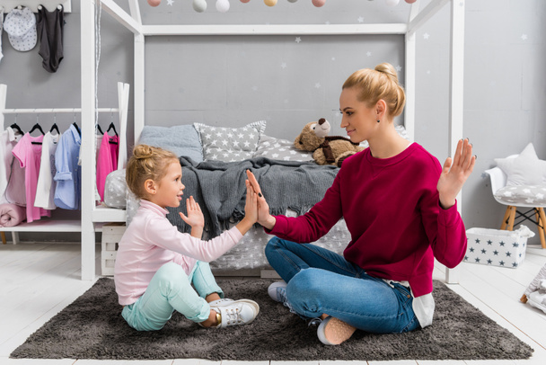 mother and daughter playing pattycake while sitting on floor - Фото, изображение