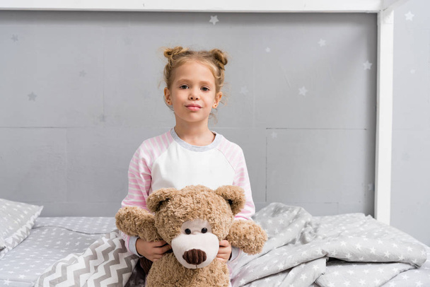 adorable little kid with teddy bear sitting on bed - Fotografie, Obrázek