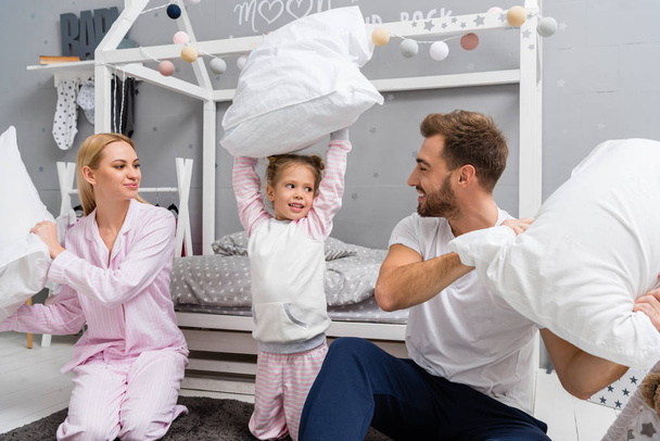 happy young family fighting with pillows in kid bedroom - Фото, изображение