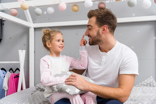 young father and happy little daughter sitting on bed in kid bedroom - Фото, изображение