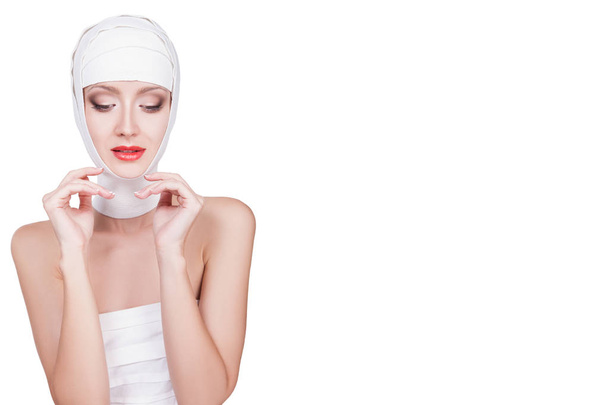 Beautiful young woman with bandages on her head, with beautiful face make-up. Lovely portrait of female face in bandages with red lipstick on her lips, isolated on white background - Valokuva, kuva