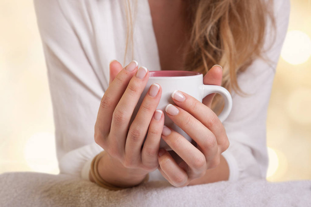 Closeup of coffee cup in female hands, blurred gentle background - 写真・画像