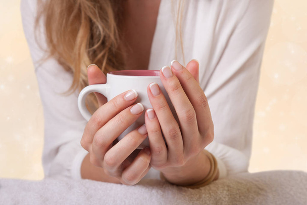 Closeup of coffee cup in female hands, blurred gentle background - Fotó, kép
