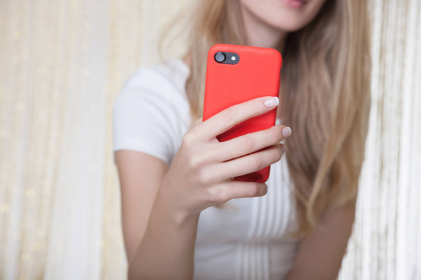 Lovely young woman wearing white dress holding red mobile phone in hands, making selfie shot - Foto, imagen