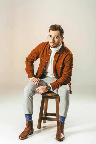 stylish man looking at camera while sitting on wooden chair, on beige - Фото, зображення