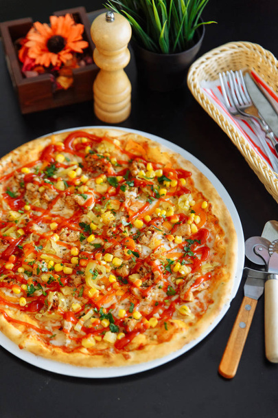 Изысканная итальянская пицца на белой тарелке с куттерии, резак для пиццы, перцовая мельница, цветок и трава в вазах
 - Фото, изображение