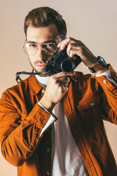 портрет модного молодого человека в очках с фотокамерой, изолированного на бежевом
  - Фото, изображение