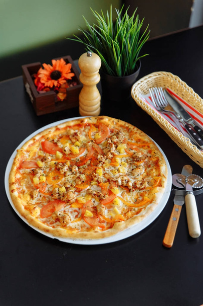 Pizza italiana gourmet su piatto bianco con taglierina, taglierina per pizza, macinapepe, fiore ed erba in vasi
 - Foto, immagini