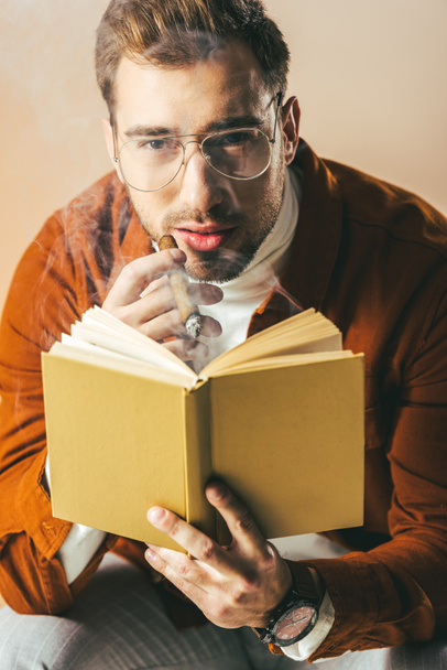 retrato de joven con cigarro y libro en las manos mirando a la cámara aislada en beige
 - Foto, imagen
