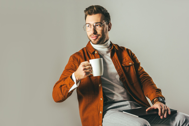 portrait of stylish man with cup of coffee in hand looking away isolated on grey - Foto, imagen