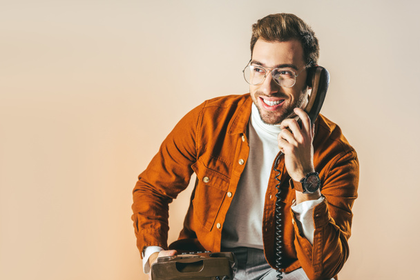 portrait of cheerful man talking on telephone isolated on beige - 写真・画像