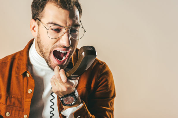 πορτρέτο του καλαίσθητο άνθρωπος ουρλιάζοντας ενώ μιλάτε στο τηλέφωνο απομονώνονται σε μπεζ - Φωτογραφία, εικόνα